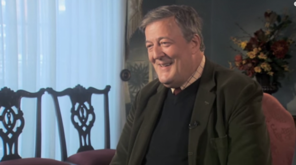 Screenshot of video appearance of Stephen Fry, seated by a window, prepared to answer a question on The Meaning of Life broadcast