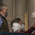 two men installing carving of elie weisel on cathedral doorway