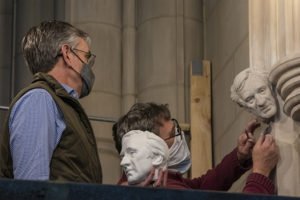 two men installing carving of elie weisel on cathedral doorway